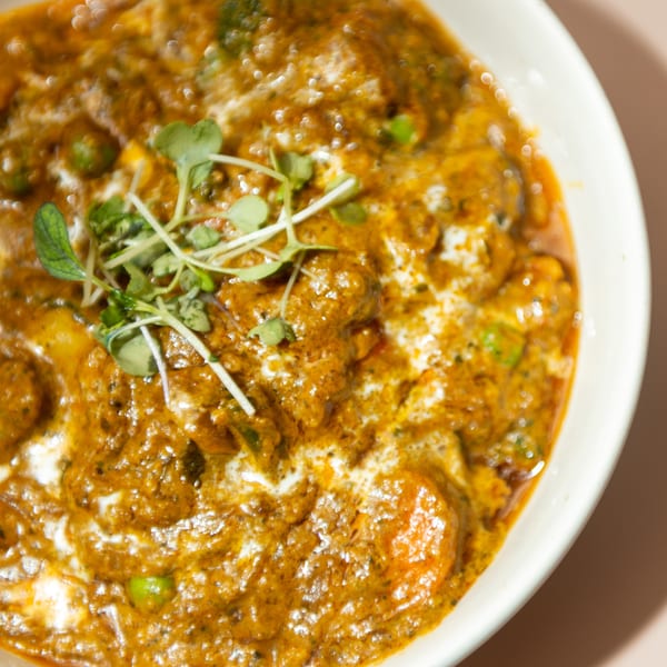 Close-up of a rich, creamy Indian curry with peas and microgreens in a white bowl.