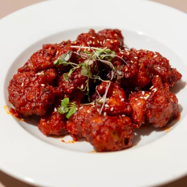 Haldi Fine Indian Cuisine's bright red chicken dish, garnished with sesame seeds and microgreens.