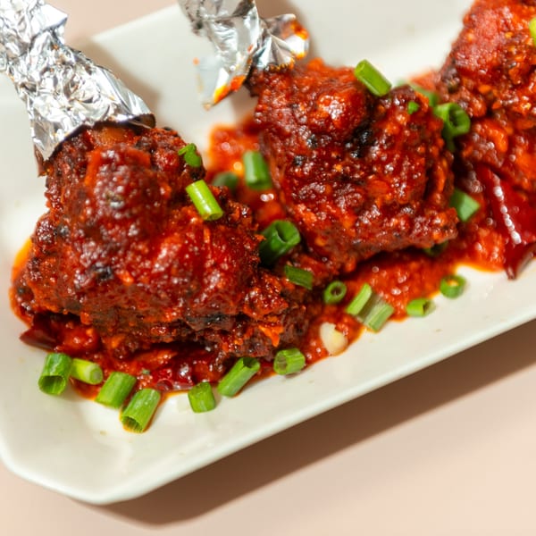 Haldi Fine Indian Cuisine's chicken lollipops, coated in a rich red sauce and garnished with green onions.
