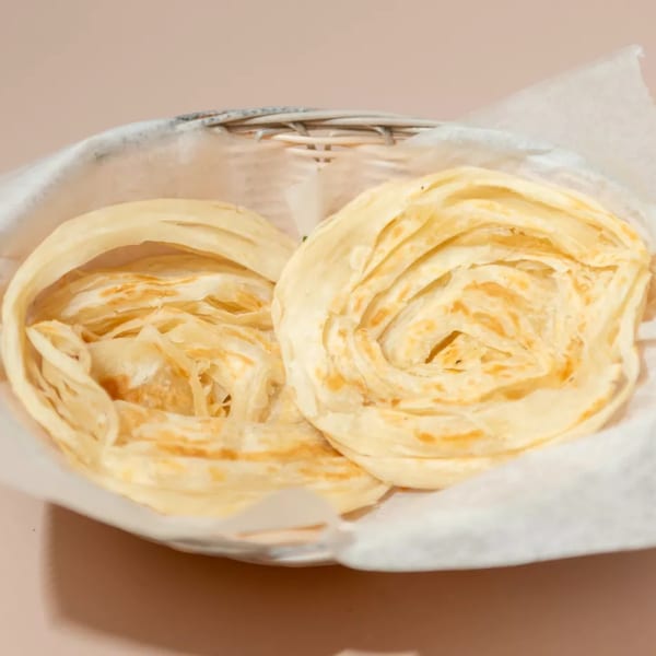 Two golden-brown, flaky Indian paratha flatbreads served in a white basket lined with parchment paper.
