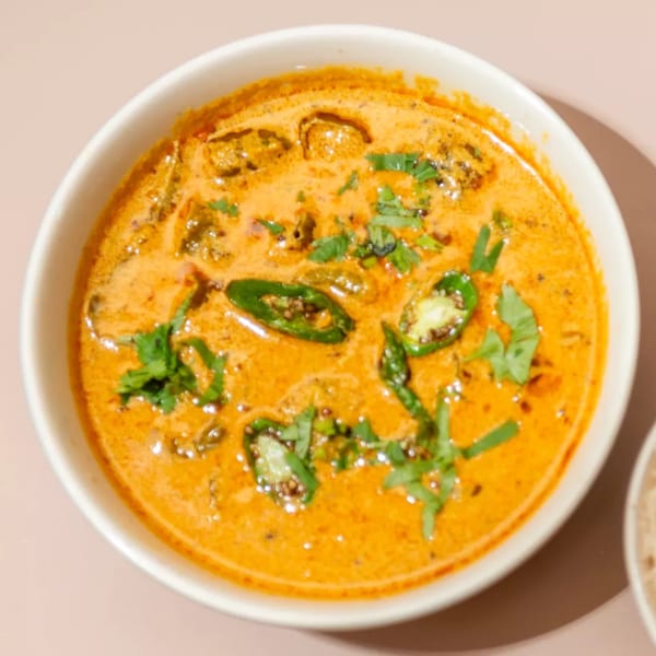 A white bowl of Haldi Fine Indian Cuisine's orange curry, garnished with green chilies and cilantro.