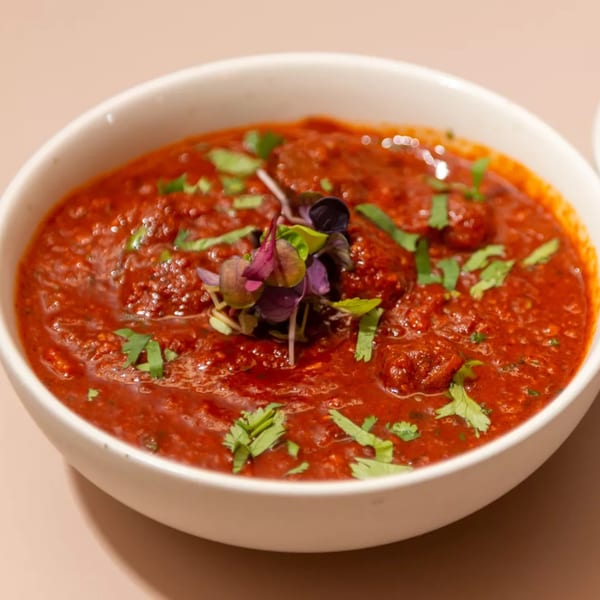A white bowl of Haldi Fine Indian Cuisine's vibrant red curry, garnished with fresh cilantro and microgreens.