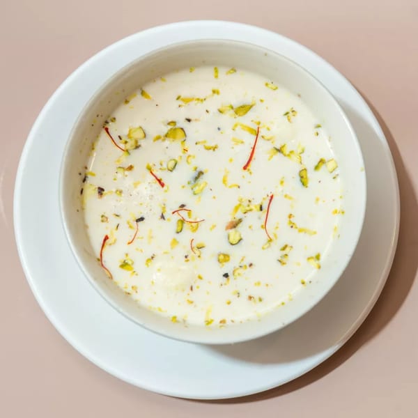 A bowl of creamy Indian dessert, Rasmalai, garnished with pistachios and saffron threads.