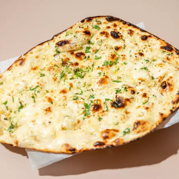 Close-up of a golden-brown garlic naan bread, topped with melted cheese and fresh green herbs.