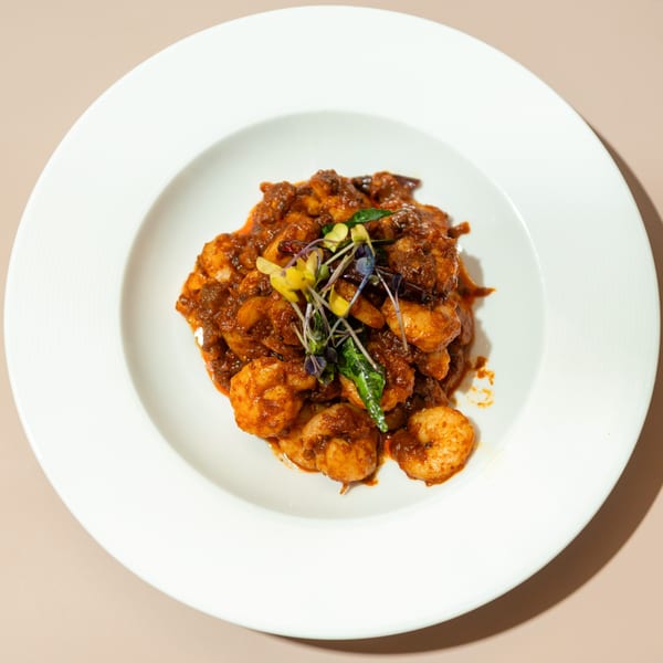 Haldi Fine Indian Cuisine's shrimp curry, garnished with microgreens, served in a white bowl.