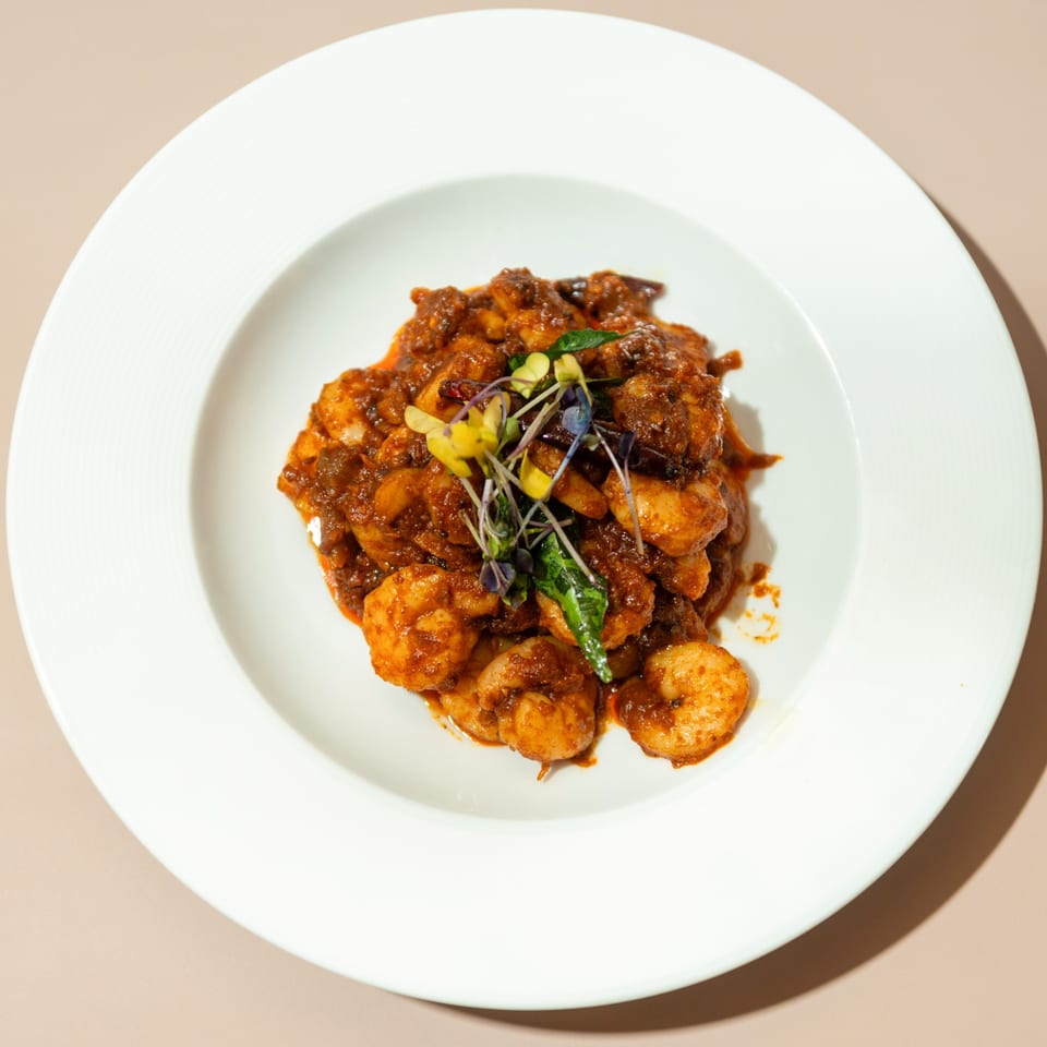 Haldi Fine Indian Cuisine's shrimp curry, garnished with microgreens, served in a white bowl.