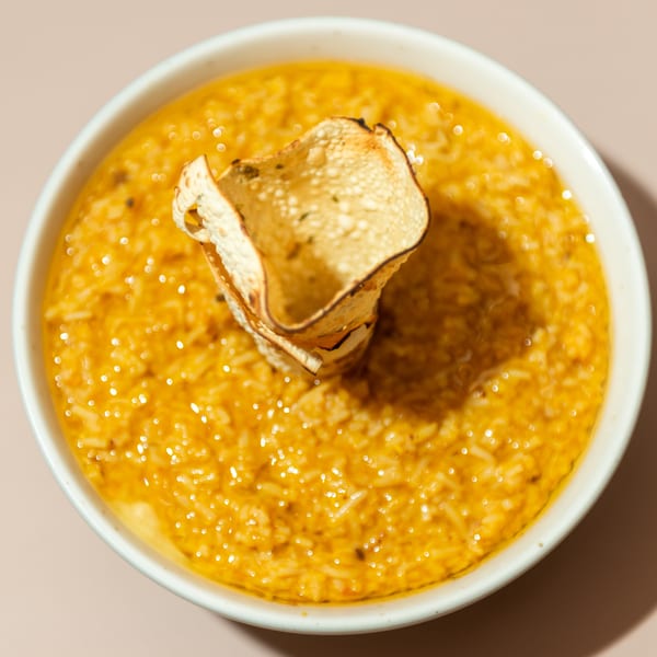 A white bowl of yellow Indian dal with a crispy papadum garnish, viewed from above.