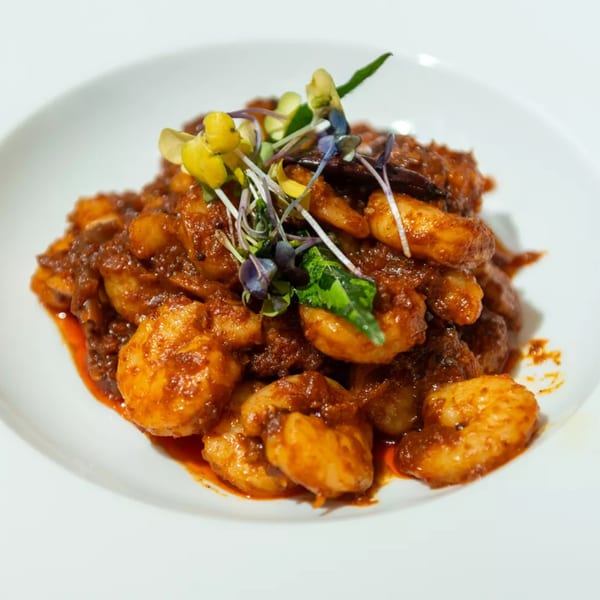 Haldi Fine Indian Cuisine's shrimp dish in a rich, red sauce, garnished with microgreens.