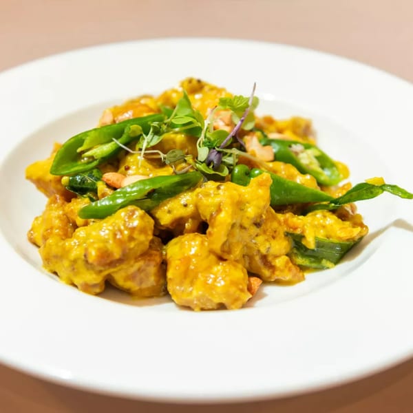 Haldi Fine Indian Cuisine's golden chicken dish with green peppers, microgreens, and nuts on a white plate.