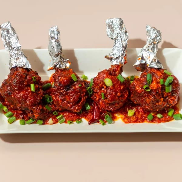 Four Haldi Fine Indian Cuisine chicken lollipops, saucy and garnished with green onions on a white plate.