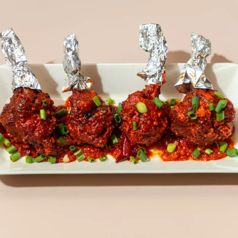 Four Haldi Fine Indian Cuisine chicken lollipops, saucy and garnished with green onions on a white plate.